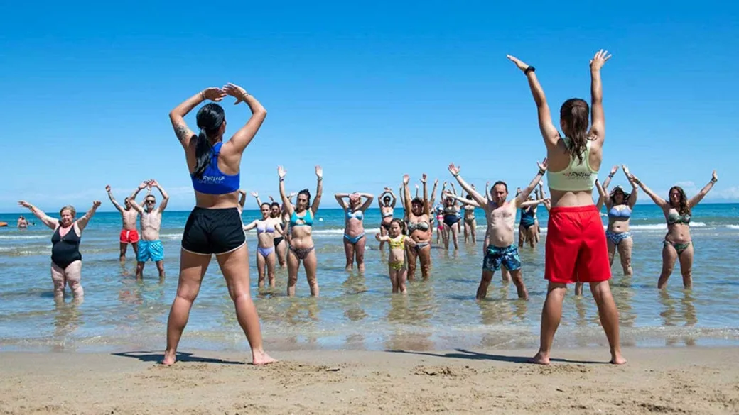 Lezione di ginnastica in acqua sulla spiaggia con animatori e gruppo di partecipanti