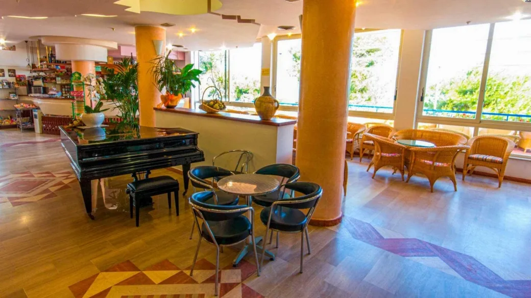 Sala interna con pianoforte a coda, tavolini, poltrone in vimini e grandi vetrate