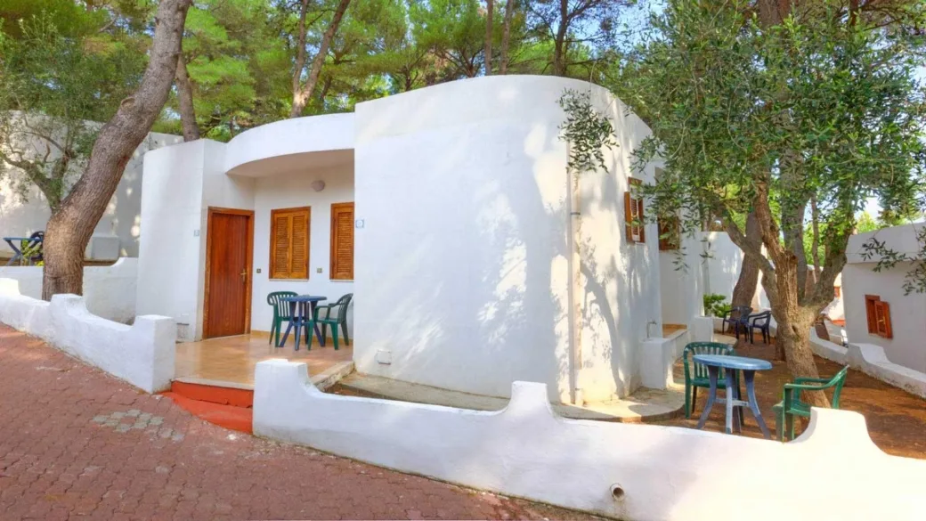 Bungalow bianco in stile mediterraneo con tavolini, sedie e ulivi nel giardino