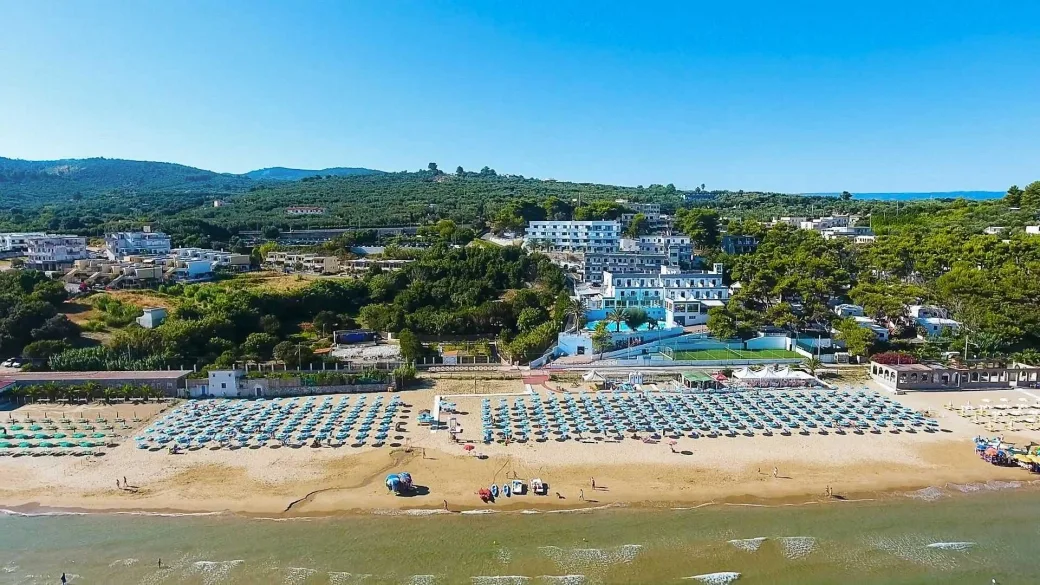 Vista aerea del complesso turistico con spiaggia attrezzata e collina verdeggiante