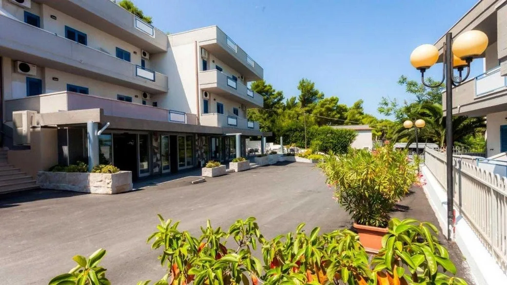 Esterno dell'hotel con ingresso, balconi e piante ornamentali lungo il vialetto