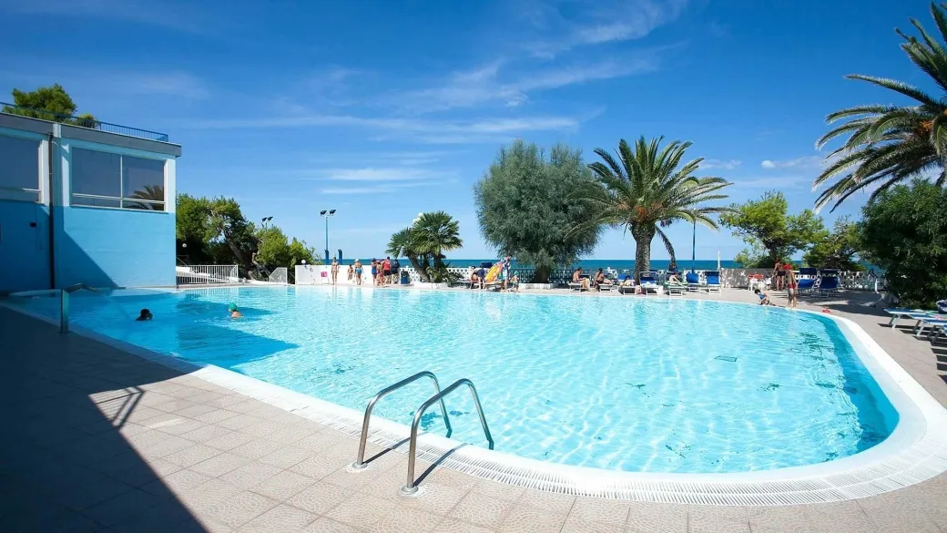 Grande piscina esterna con palme, lettini e vista sul mare