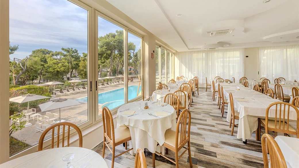 Sala ristorante luminosa con tavoli apparecchiati e vista sulla piscina