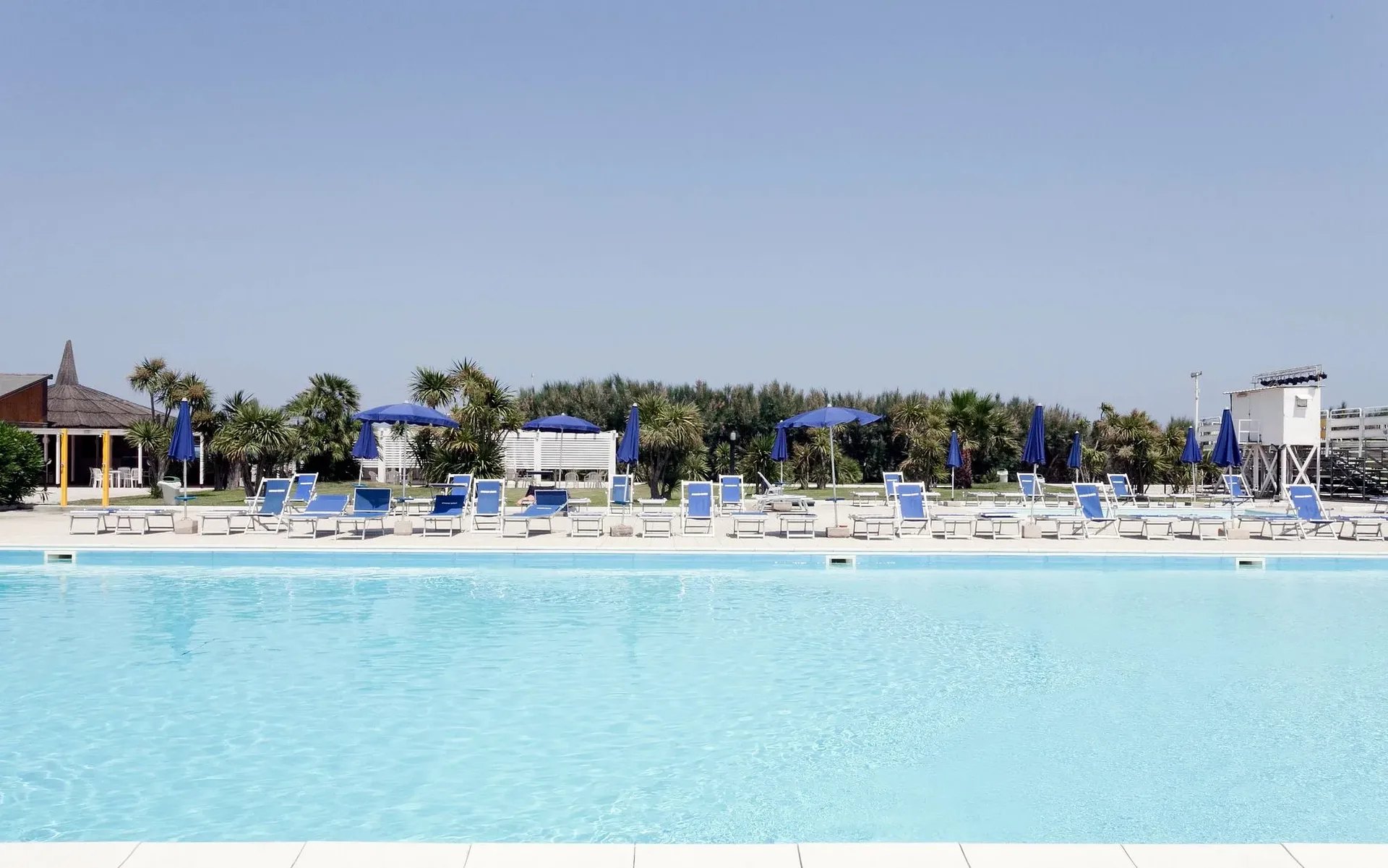 Piscina panoramica con lettini e ombrelloni blu circondata da vegetazione mediterranea