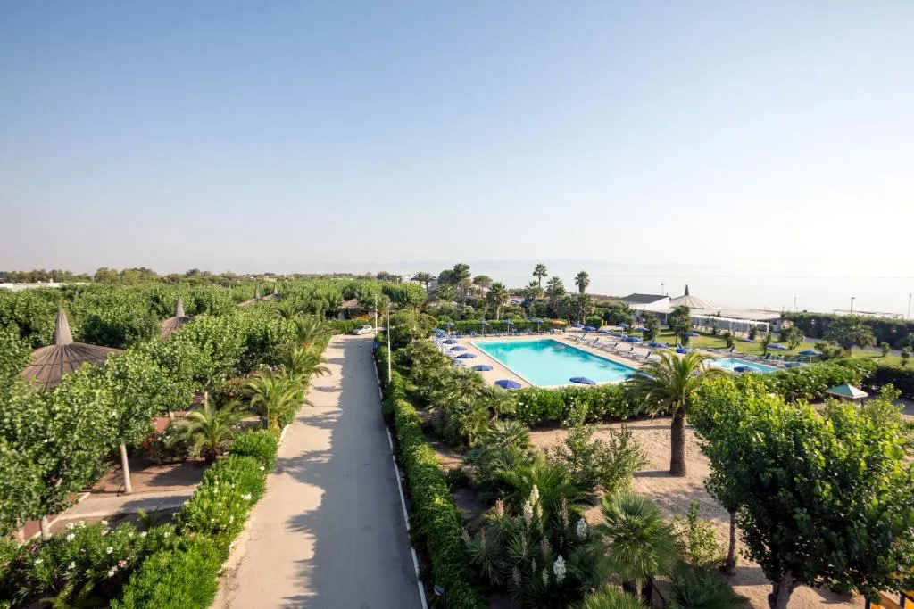 Vista aerea del viale del resort con piscina, giardini rigogliosi e mare all'orizzonte