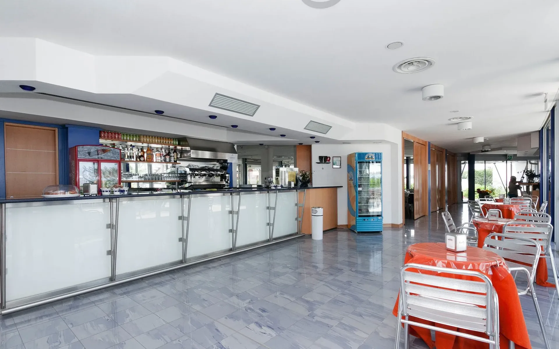 Area bar interna con bancone, tavolini rossi e sedie in metallo
