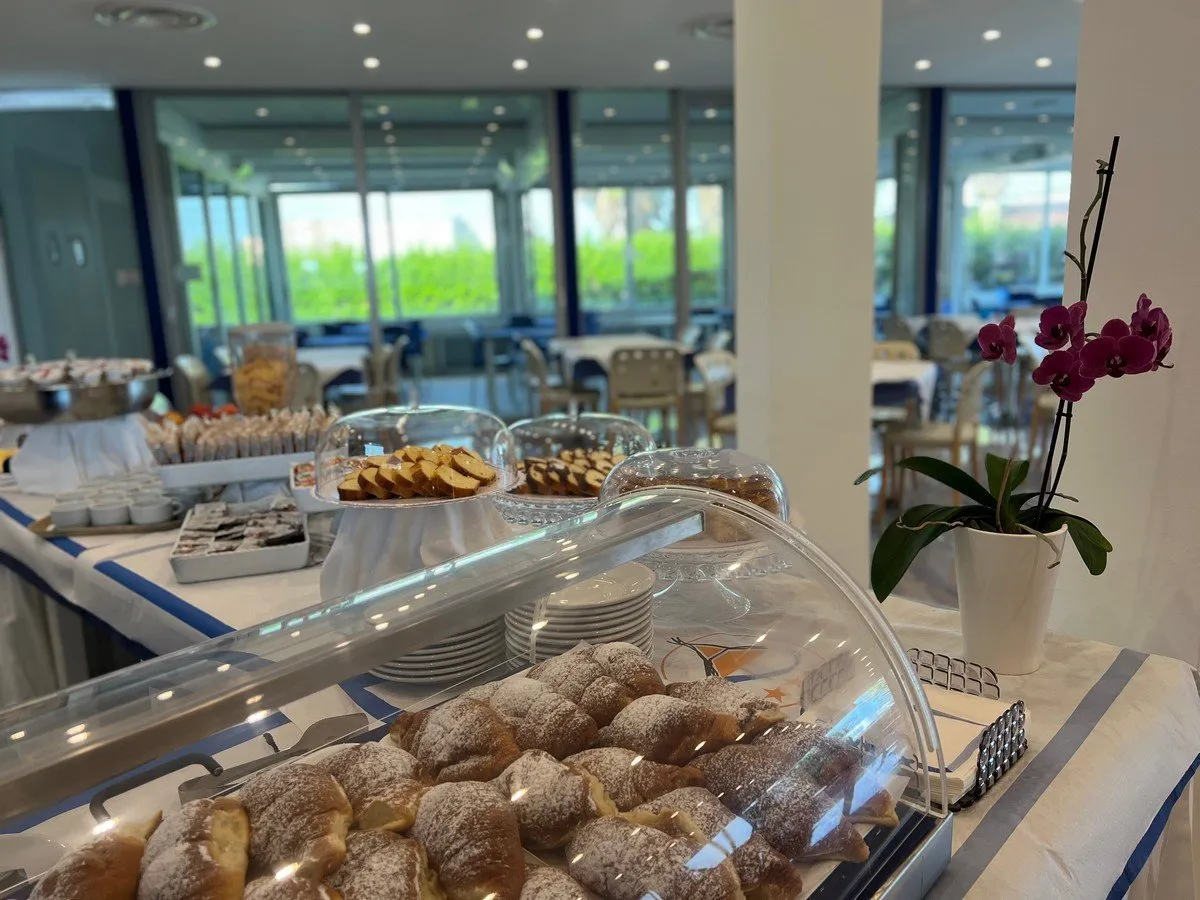 Buffet colazione con cornetti, dolci e sala ristorante sullo sfondo