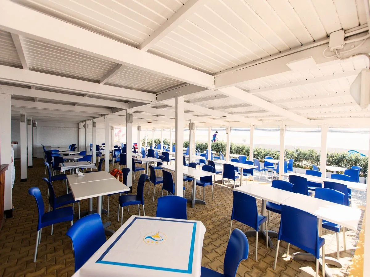 Sala ristorante coperta con tavoli, sedie blu e vista sulla spiaggia