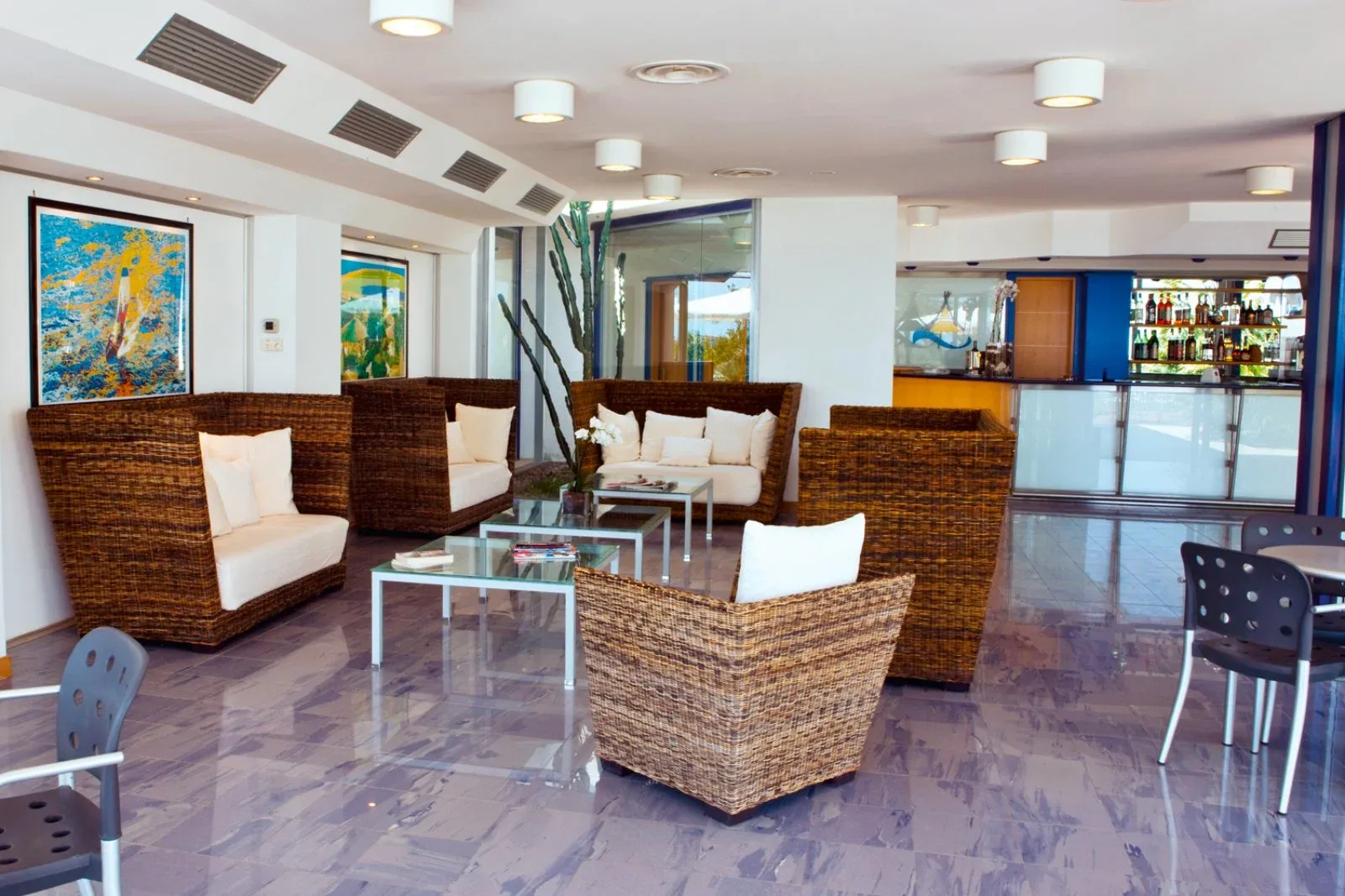 Lounge dell'hotel con poltrone in vimini, cuscini bianchi e bancone bar