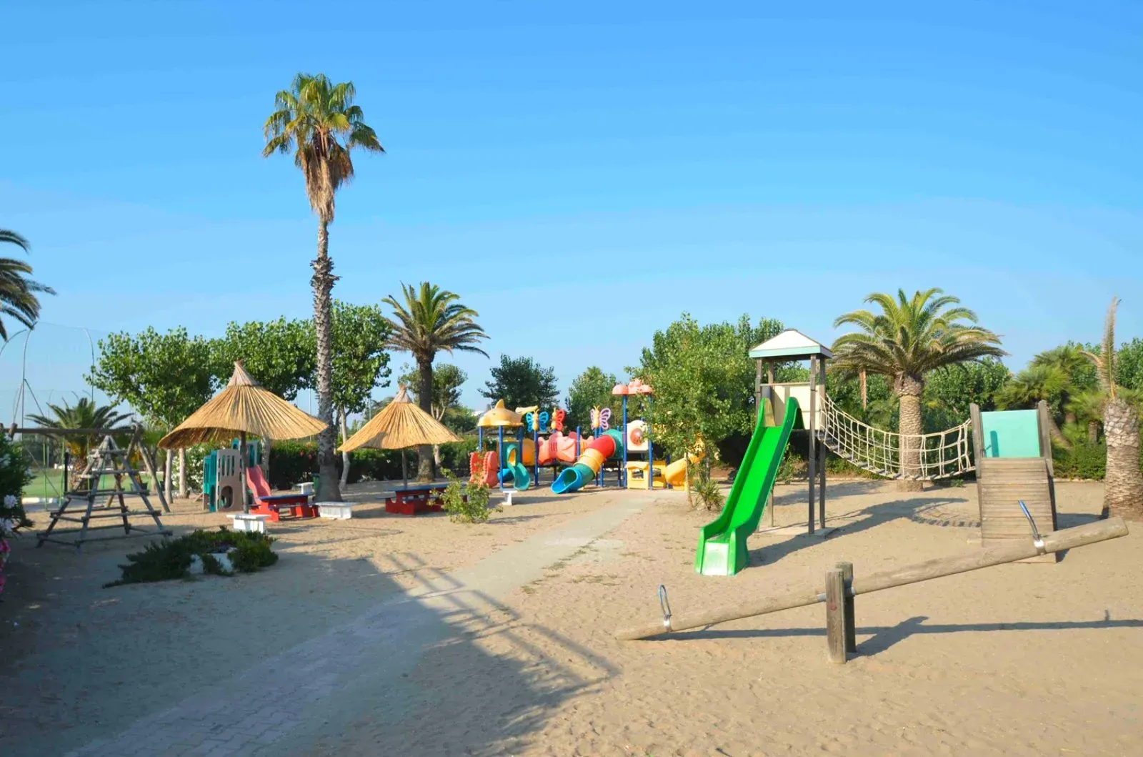 Area giochi per bambini con scivoli, altalene e ponte di corda tra le palme