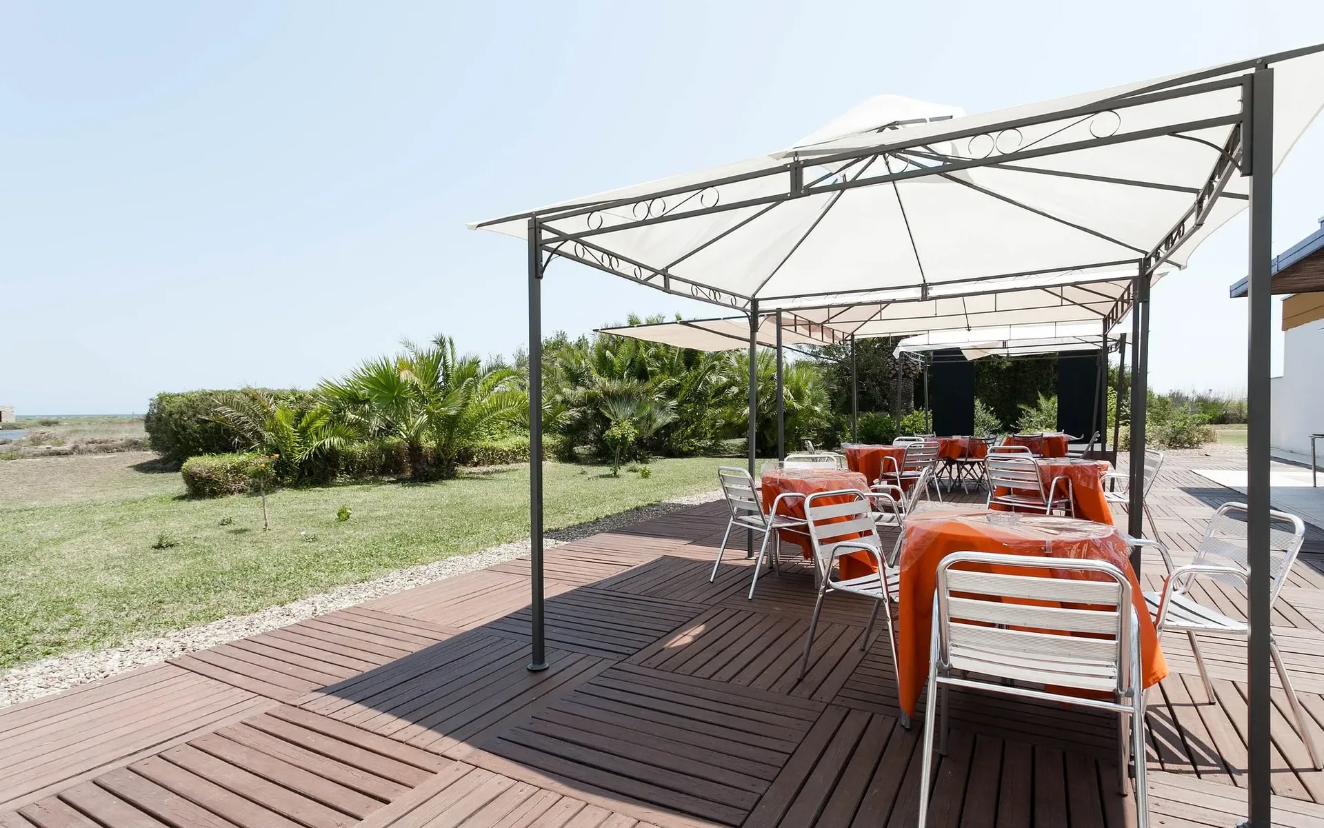 Terrazza esterna con gazebo, tavoli con tovaglie arancioni e giardino