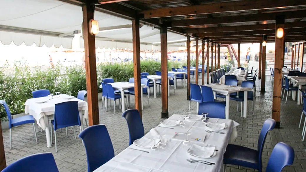 Ristorante all'aperto sotto pergolato in legno con tavoli apparecchiati e sedie blu