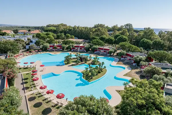 Veduta aerea della grande piscina a forma sinuosa con isolette di palme e ombrelloni rossi