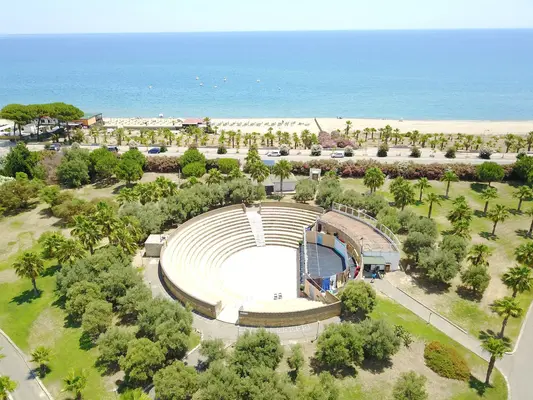 Anfiteatro all'aperto immerso tra palme e ulivi con la spiaggia sullo sfondo