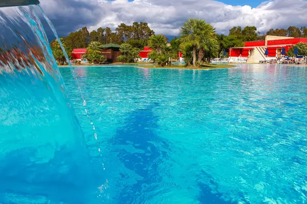 Piscina con cascata d'acqua e isolette di palme, edifici rossi del resort sullo sfondo