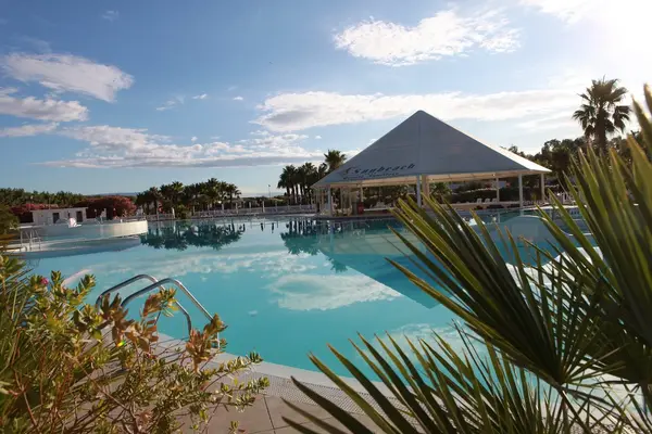 Piscina del resort con gazebo a piramide e palme riflesse sull'acqua