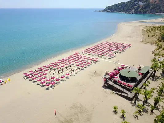 Spiaggia sabbiosa con file di ombrelloni rosa e chiosco bar in legno vista mare
