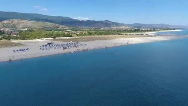 Spiaggia sabbiosa con ombrelloni e mare azzurro tra le colline