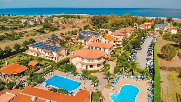 Vista aerea del villaggio turistico con piscine, edifici dai tetti arancioni e mare sullo sfondo