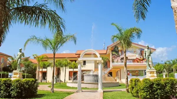 Ingresso del villaggio con fontana, arco classico e statue tra le palme