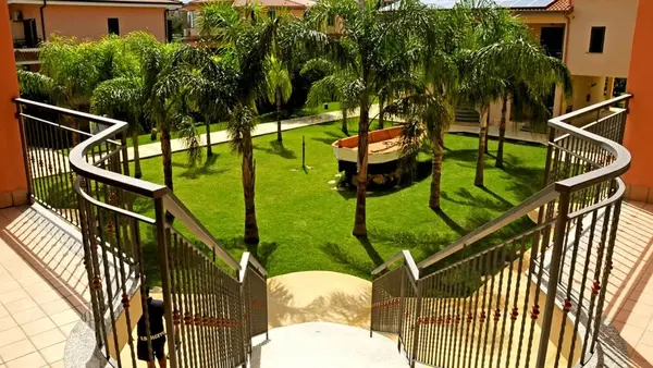 Cortile interno con palme, prato verde e barca decorativa visto dalla scalinata