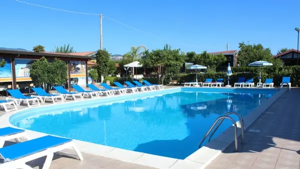 Piscina con lettini blu e ombrelloni circondata da vegetazione