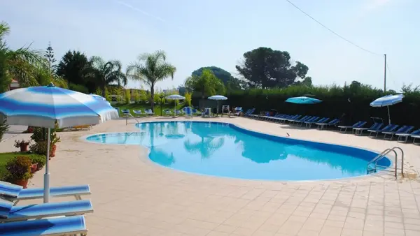 Piscina con lettini blu e ombrelloni a righe circondata da alberi