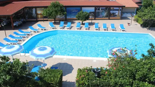 Piscina con lettini blu, ombrelloni e edificio con vetrate decorate