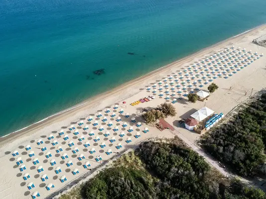 Veduta aerea di spiaggia sabbiosa con ombrelloni bianchi e lettini blu lungo il mare turchese