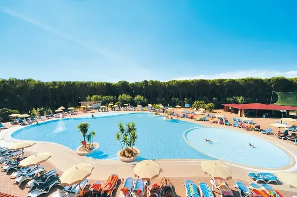Grande piscina laguna con isolotti di palme, lettini colorati e ombrelloni immersa nella pineta
