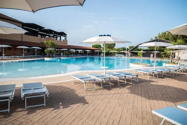 Bordo piscina con lettini e ombrelloni bianchi su pavimentazione in mattoni