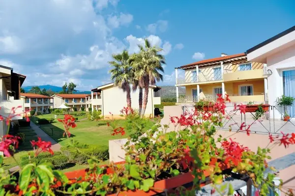 Giardino fiorito del resort con palme, prato verde ed edifici gialli a due piani