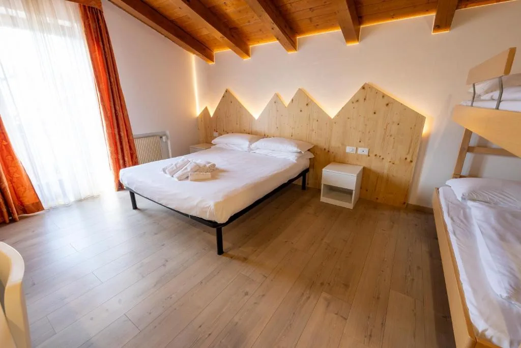 Camera luminosa con letto matrimoniale, testiera in legno a forma di montagne e travi a vista