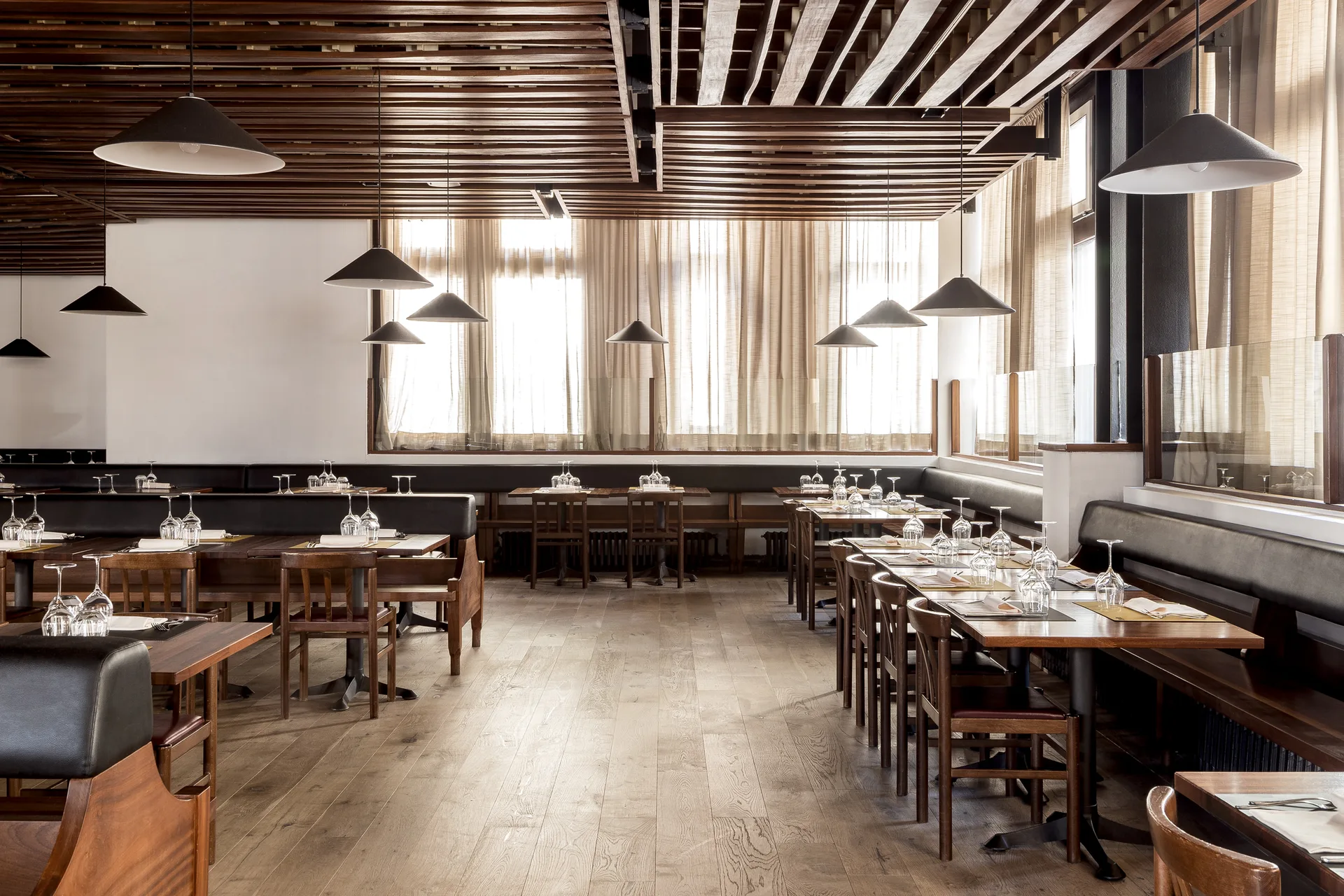 Sala ristorante con tavoli in legno apparecchiati, panche e lampade a sospensione scure