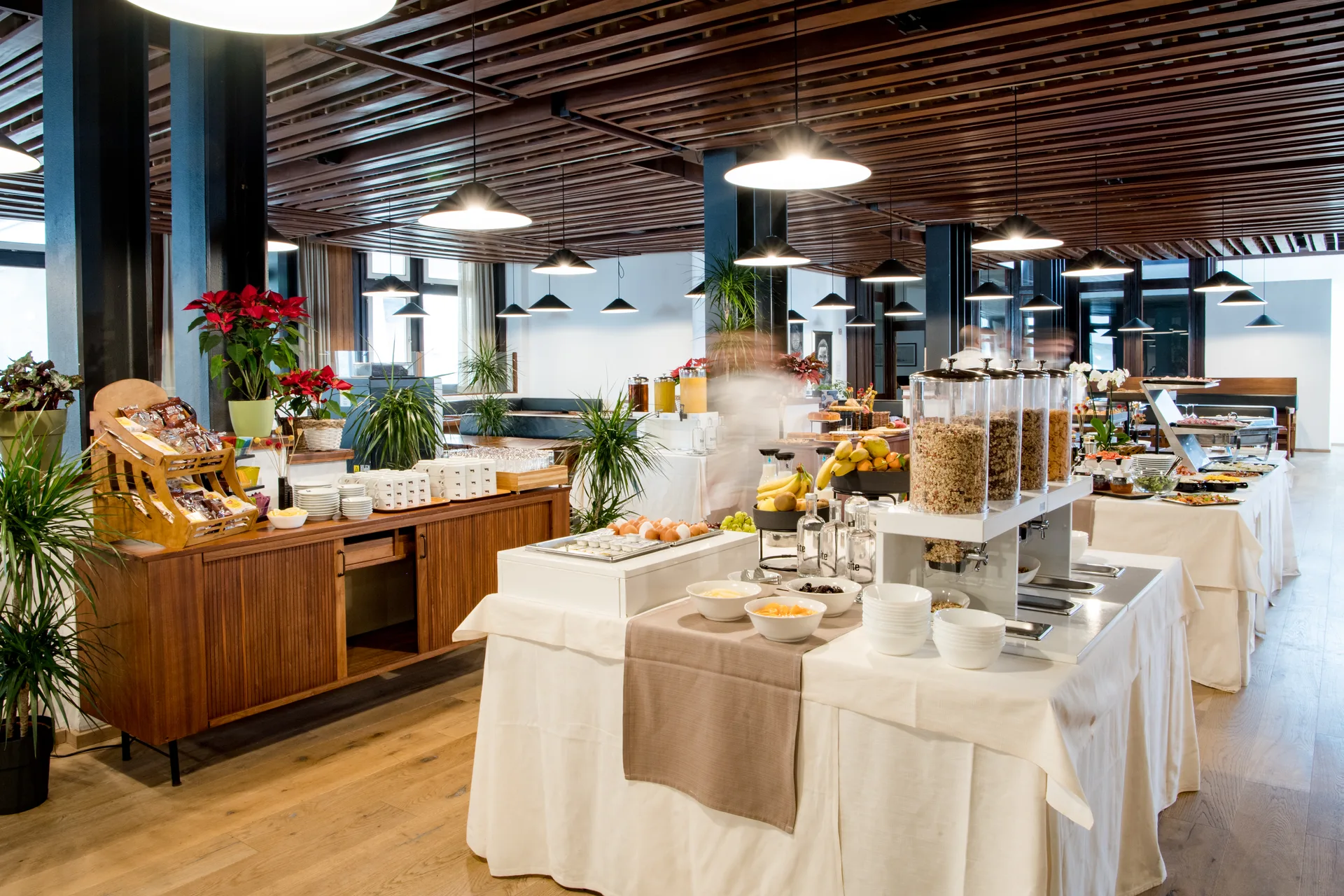 Buffet della colazione con cereali, frutta fresca, pane e bevande in sala con soffitto a doghe di legno
