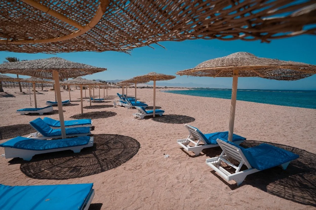 Spiaggia sabbiosa con lettini blu e ombrelloni in paglia affacciati sul mare azzurro