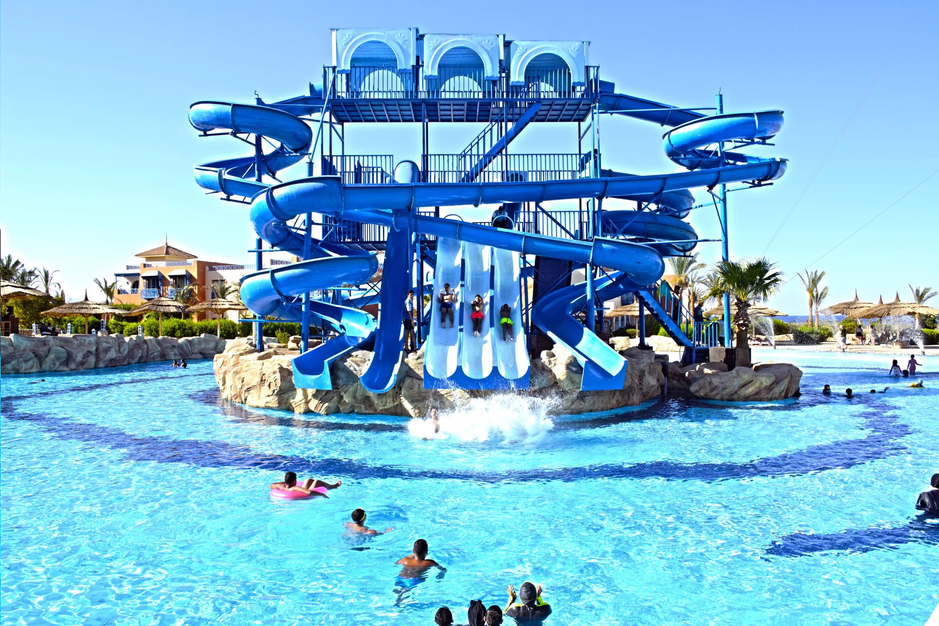 Grande torre di scivoli acquatici blu con bagnanti in piscina sotto il cielo azzurro