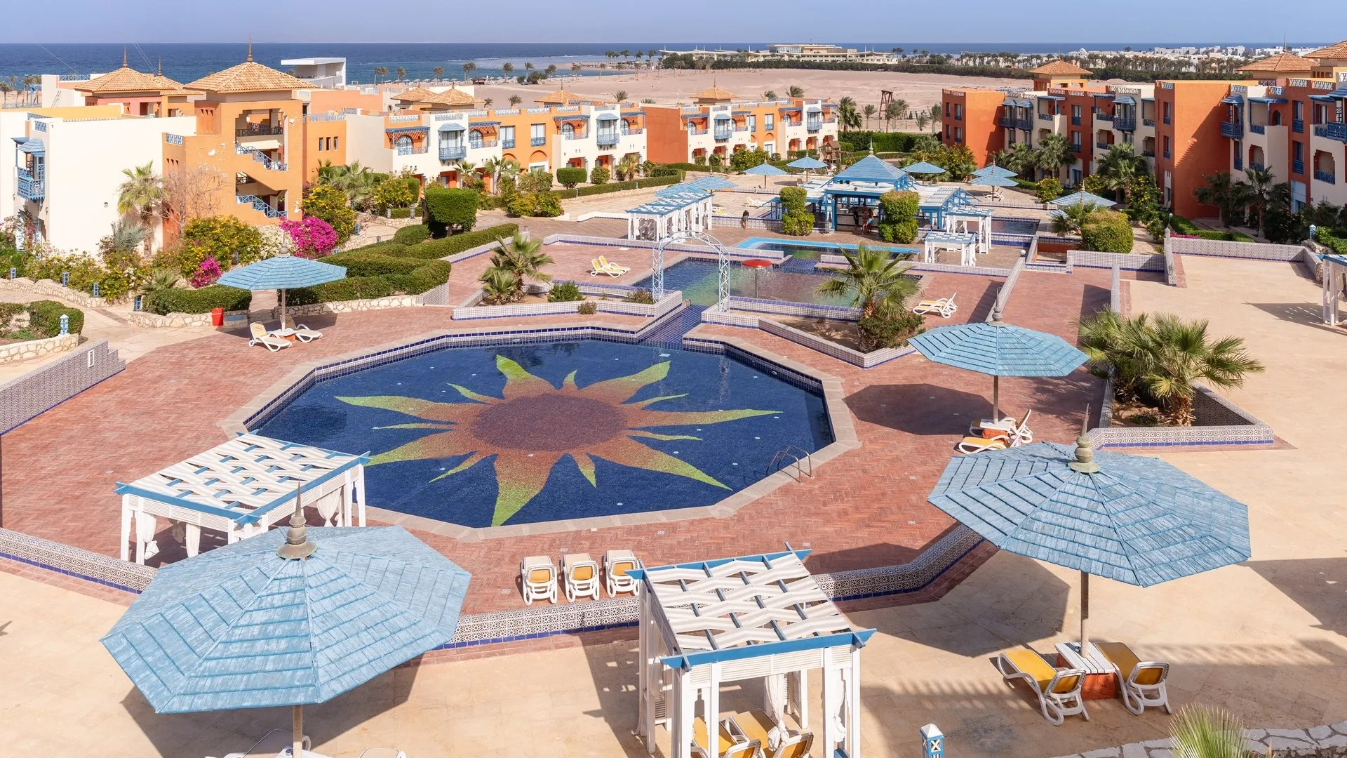 Piscina decorata con mosaico a forma di sole, ombrelloni blu e vista sul mare sullo sfondo
