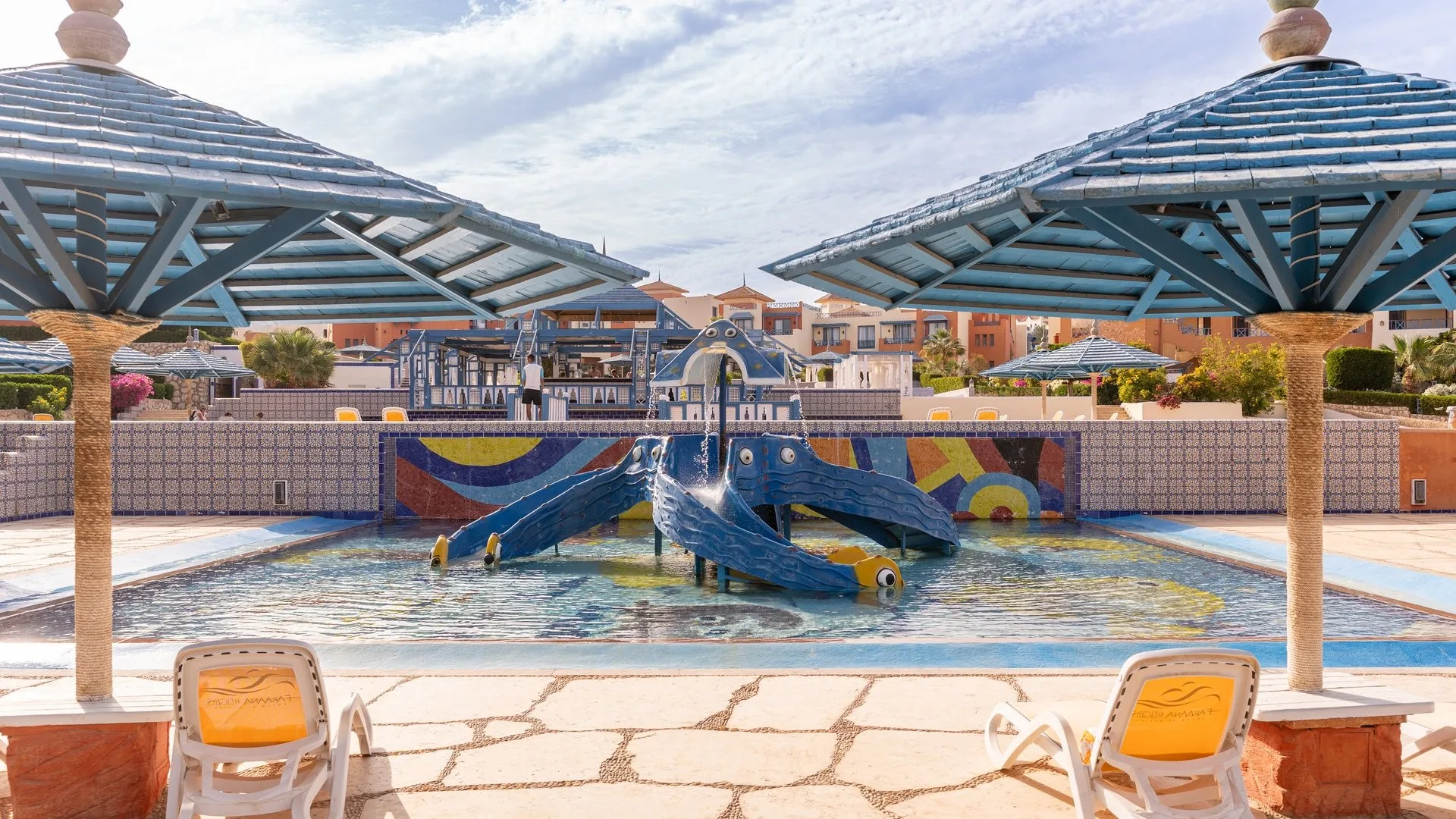 Piscina per bambini con scivoli colorati a forma di animali marini e ombrelloni blu in legno