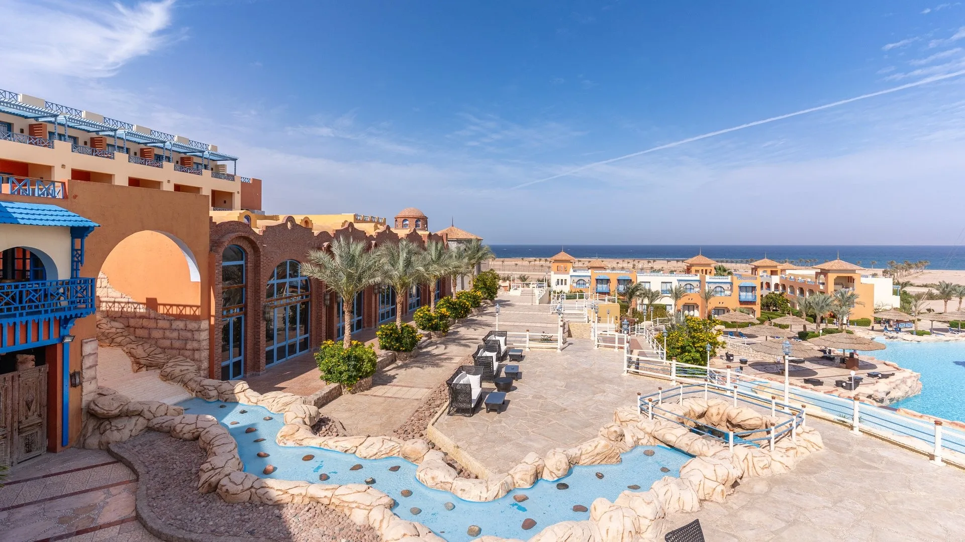 Terrazza del resort con corso d'acqua decorativo, palme e vista sul mare sullo sfondo