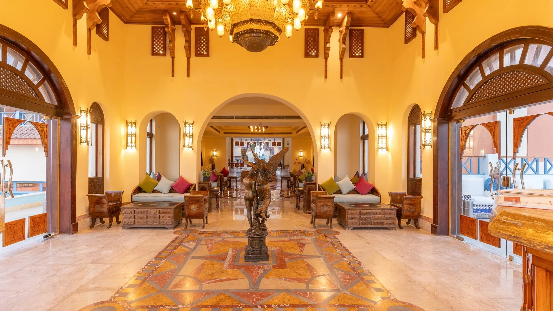 Hall del resort con statua in bronzo, lampadario dorato, divani colorati e pavimento intarsiato