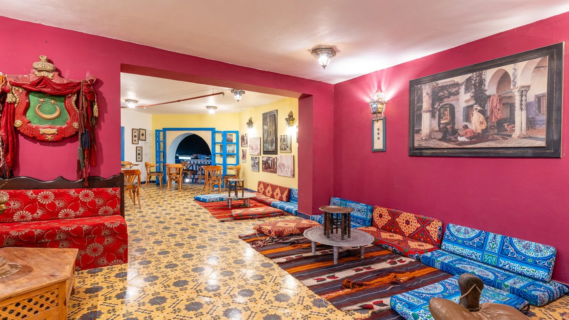 Salone in stile arabo con pareti rosse, divani colorati, cuscini decorati e tavolini bassi