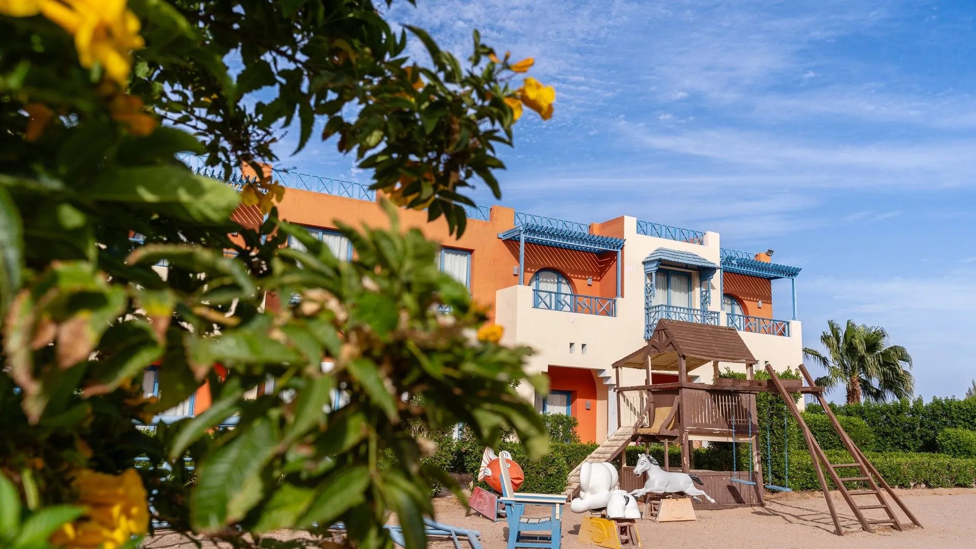 Esterno di un edificio del resort con parco giochi per bambini e vegetazione fiorita in primo piano