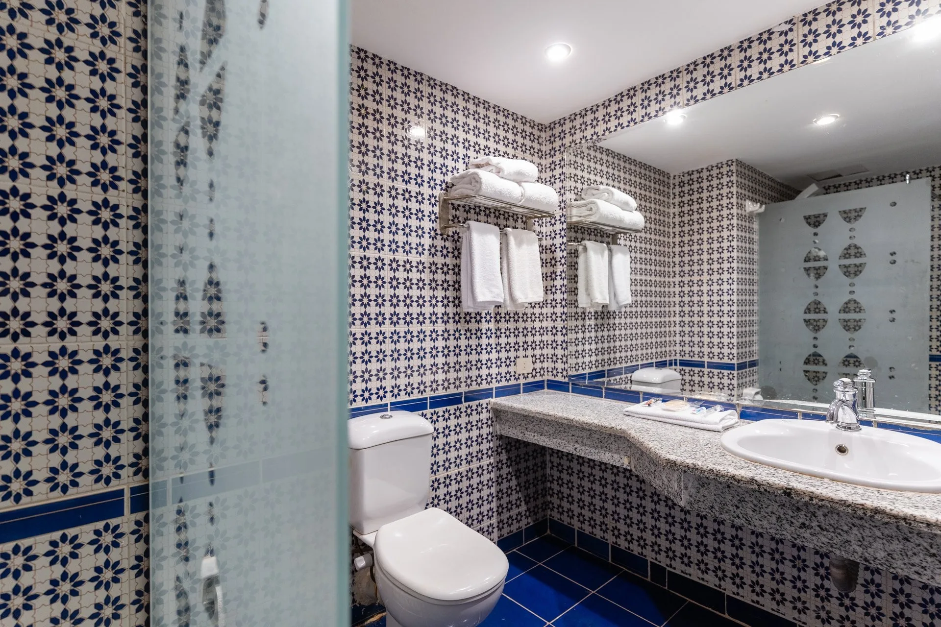 Bagno della camera con piastrelle blu a motivi decorativi, lavabo, specchio e asciugamani