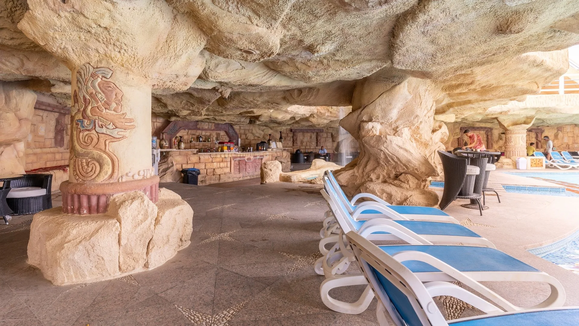 Bar in grotta artificiale con colonne decorate a tema maya, lettini e bancone