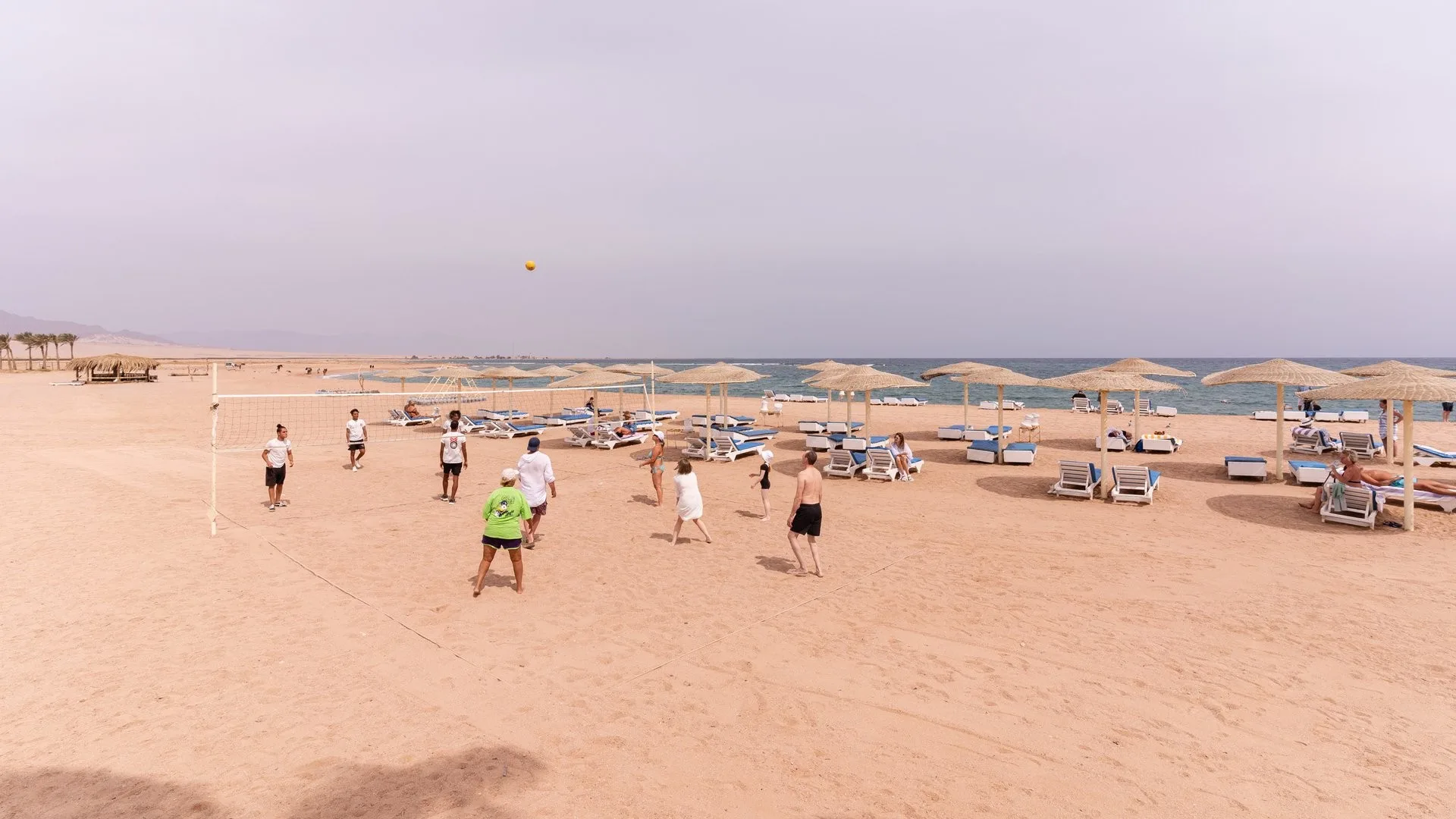 Partita di beach volley sulla spiaggia del resort con lettini e ombrelloni in paglia
