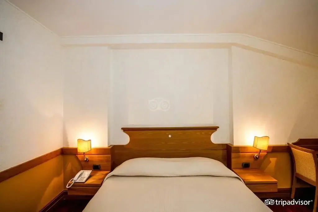 Camera con letto singolo, testiera in legno e lampade da comodino accese