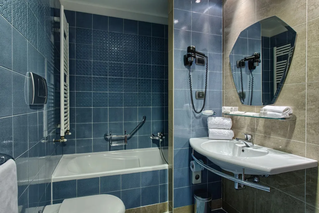 Bagno con piastrelle blu, vasca, lavabo e specchio con asciugacapelli