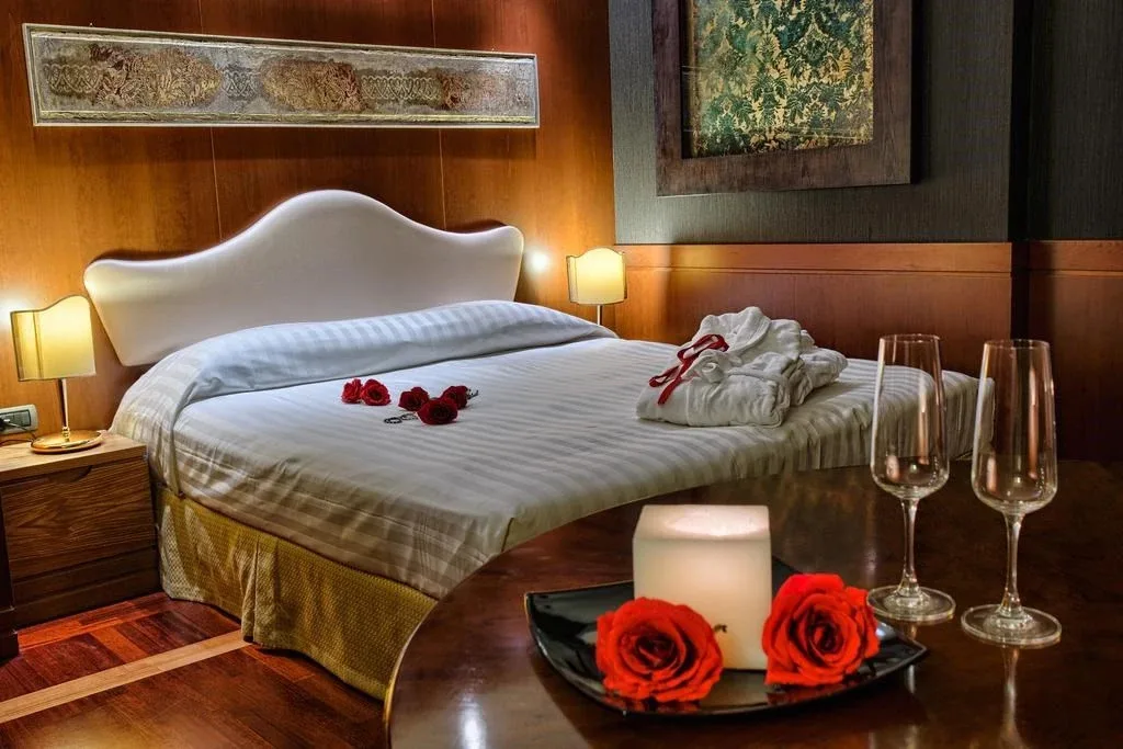 Camera romantica con letto decorato con rose rosse, accappatoio e calici di spumante
