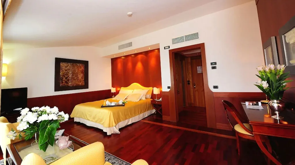 Camera spaziosa con letto matrimoniale, copriletto giallo, poltrone e pavimento in legno